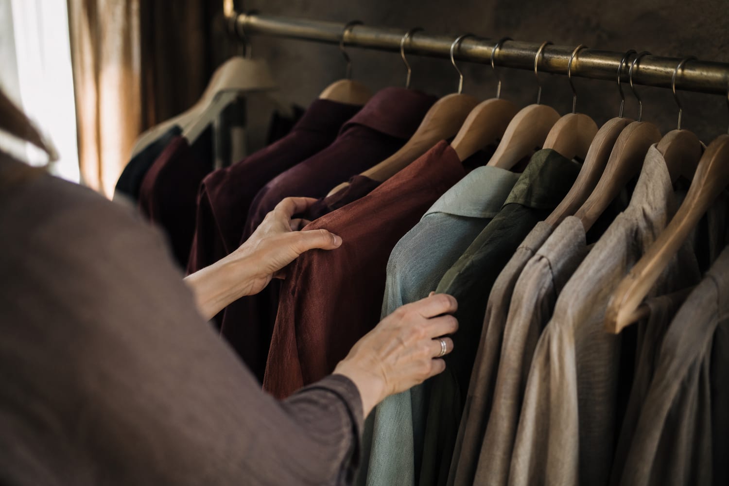 Hands considering tailored coats on a brass clothing rail