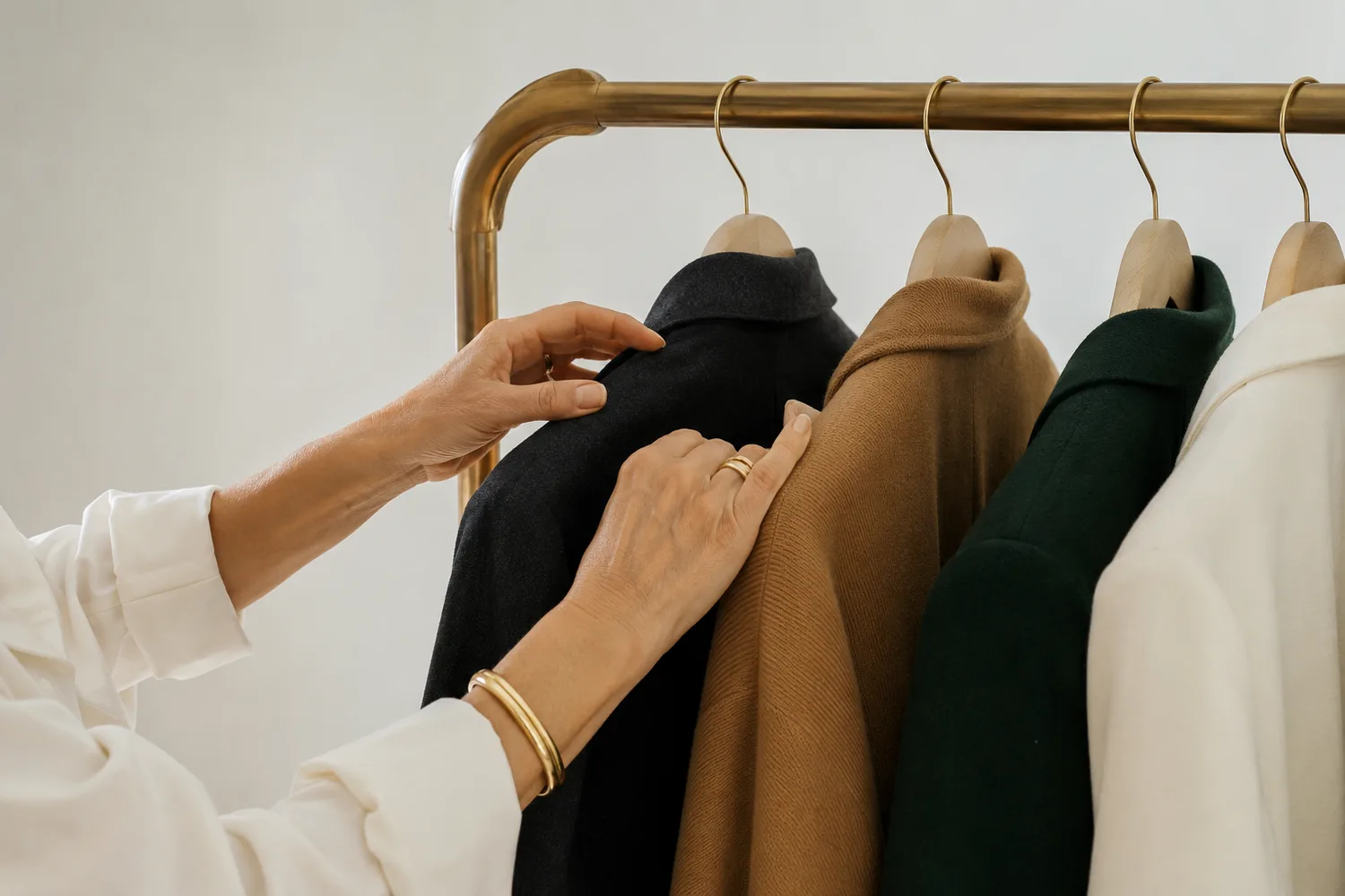 Hands considering tailored coats on a brass clothing rail